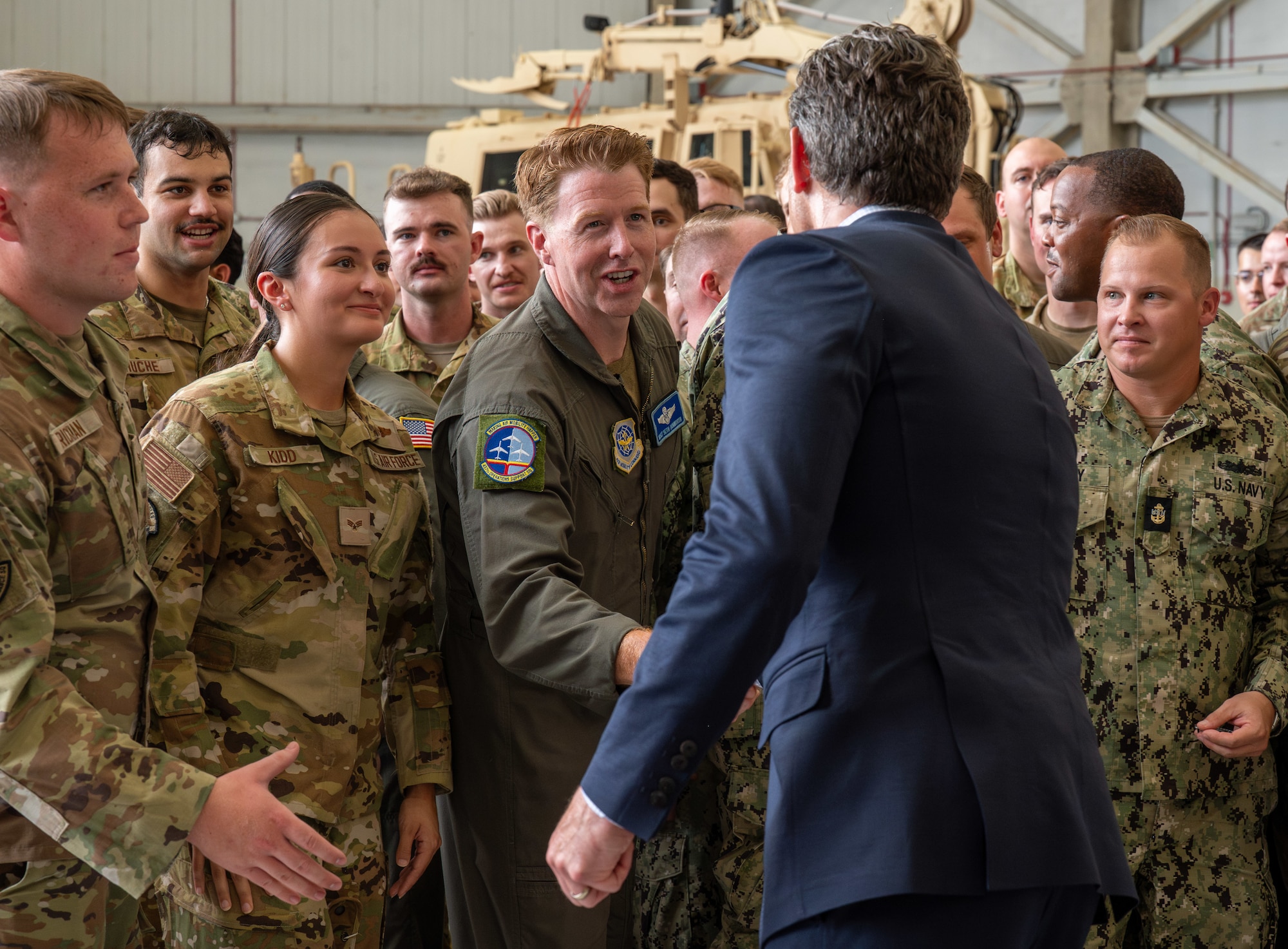 A man shakes hands with a group of service members in a crowd.