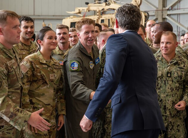 A man shakes hands with a group of service members in a crowd.