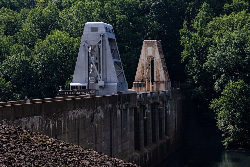 Two large steel structures sit atop a dam in a wooded area.