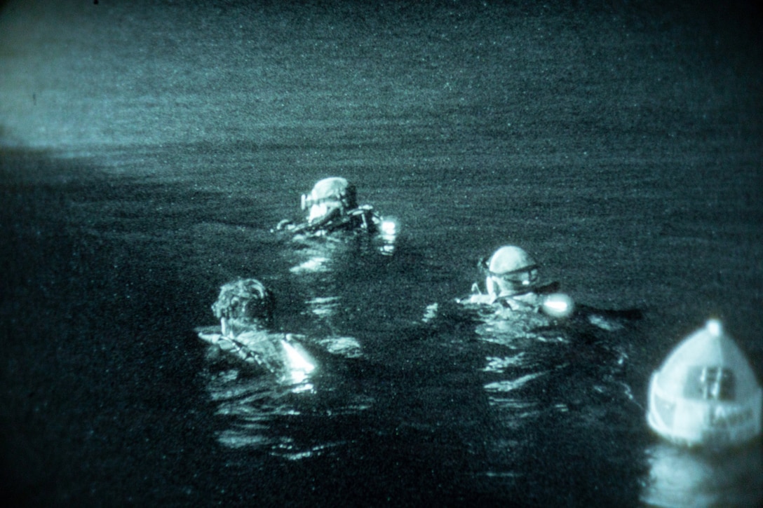 Three people wearing goggles swim in a triangle formation at night. A buoy floats behind them.