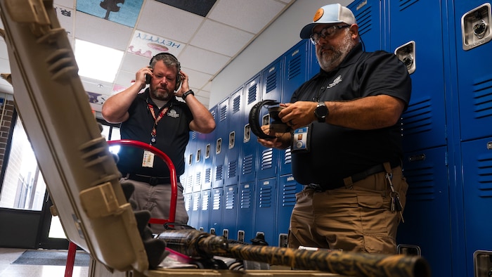 A photo of two men in a hallway equipping hearing protection gear.