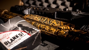 A photo of an M4 rifle, a 12-gauge shotgun and a box of blank ammunition.