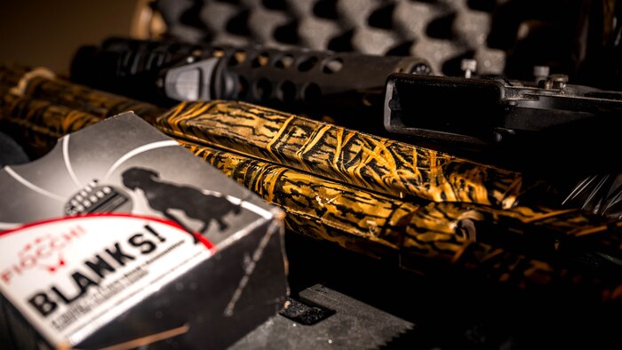 A photo of an M4 rifle, a 12-gauge shotgun and a box of blank ammunition.