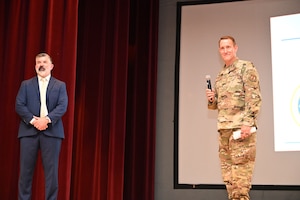 A man in a suit and a man in military uniform stand on a stage
