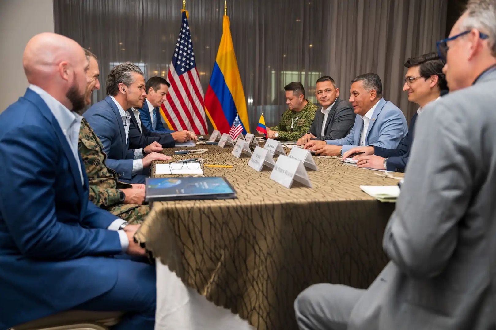 People in civilian attire and military uniforms sit around a table indoors.