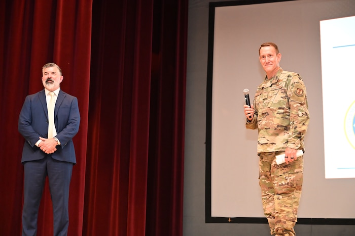 A man in a suit and a man in military uniform stand on a stage