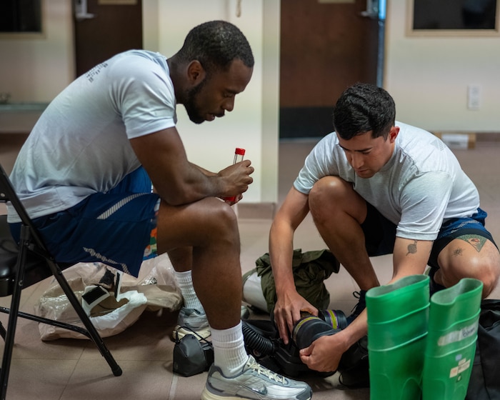 Two men in Air Force physical training gear, assemble a motorized breathing machine.