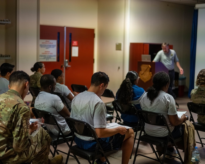 A group of U.S. Air Force Airmen sit in chair during a class lesson.