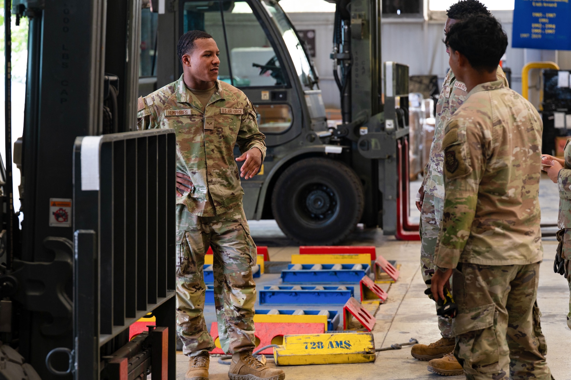 A man stands in front of a forklift talking to two others in uniform.