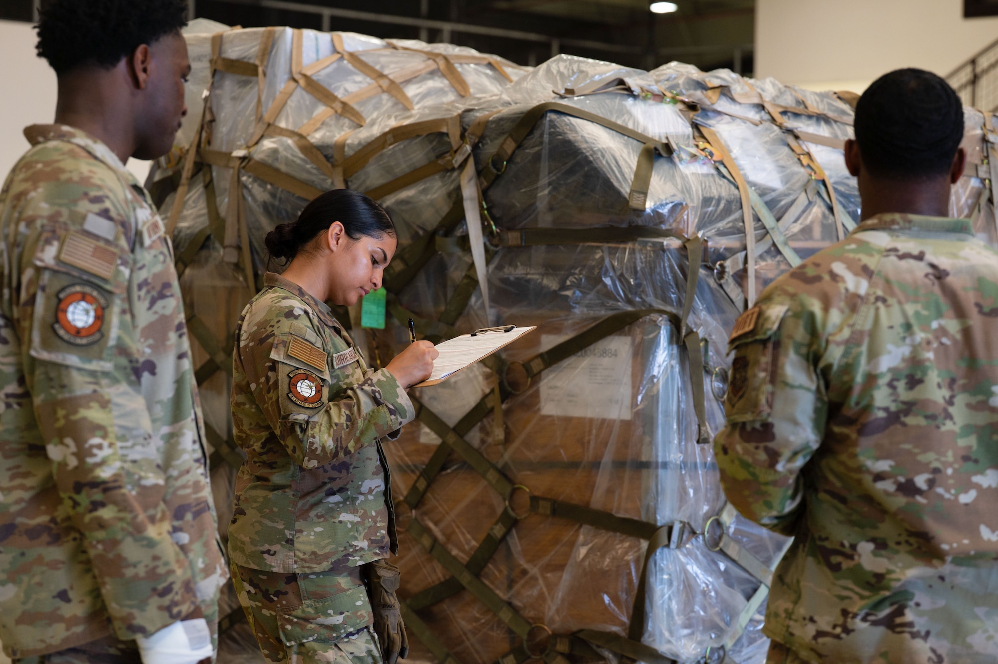 A group of airmen stand in front of a pallet and take notes.