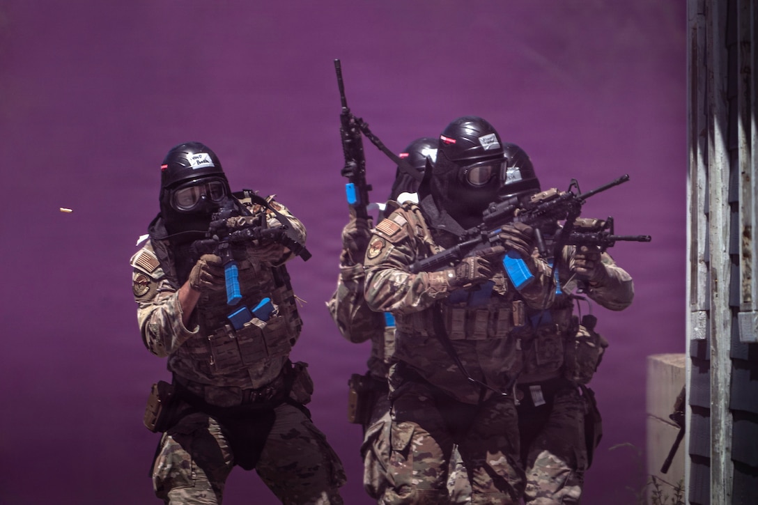 Several airmen wearing gas masks wield rifles outside with purple smoke filling the air.