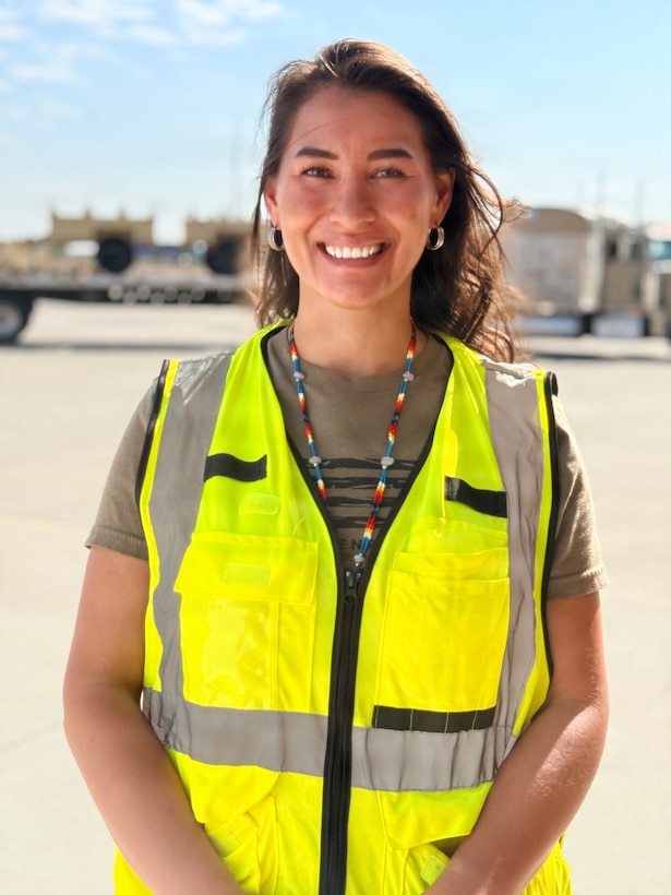 Woman wearing a yellow safety jacket standing in front of military truck.