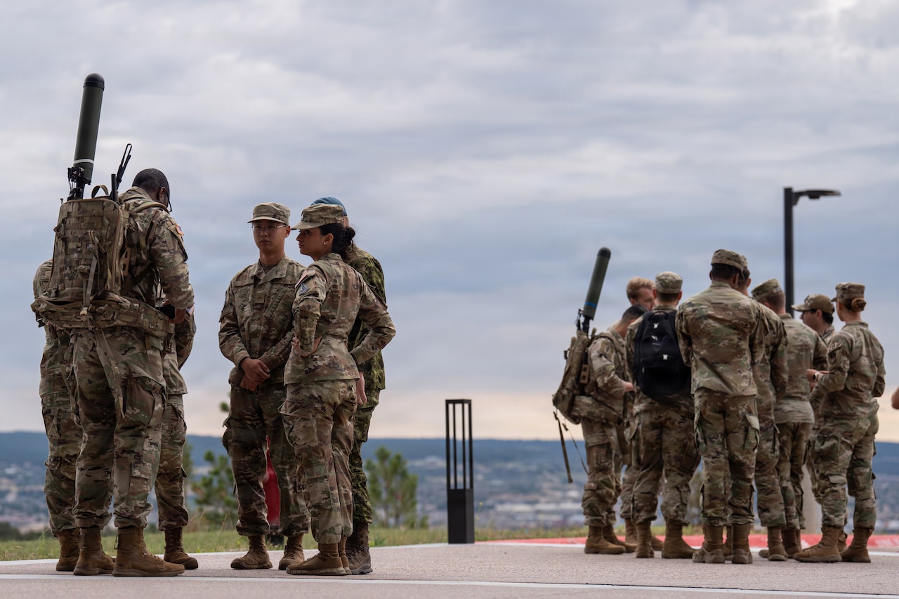 People wearing camouflage military uniforms stand in two circles while watching equipment demonstrations.