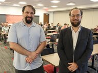 A photo of two middle age me standing in front of their classroom.