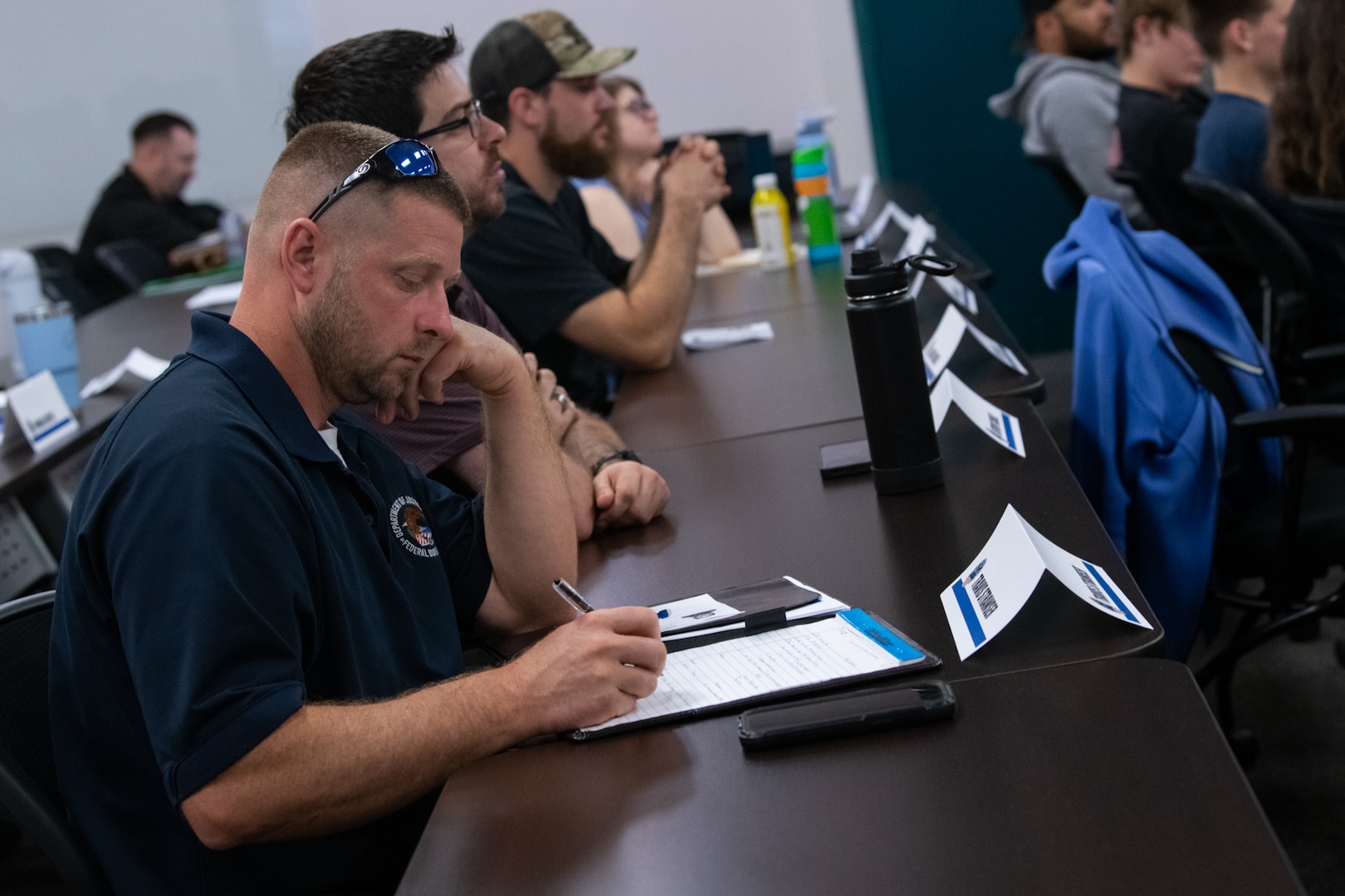 A man sits at a table in a conference room writing on a pad of paper.
