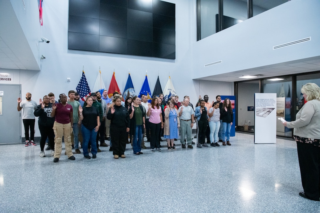 A large group of people stand in a building lobby in front of flags.