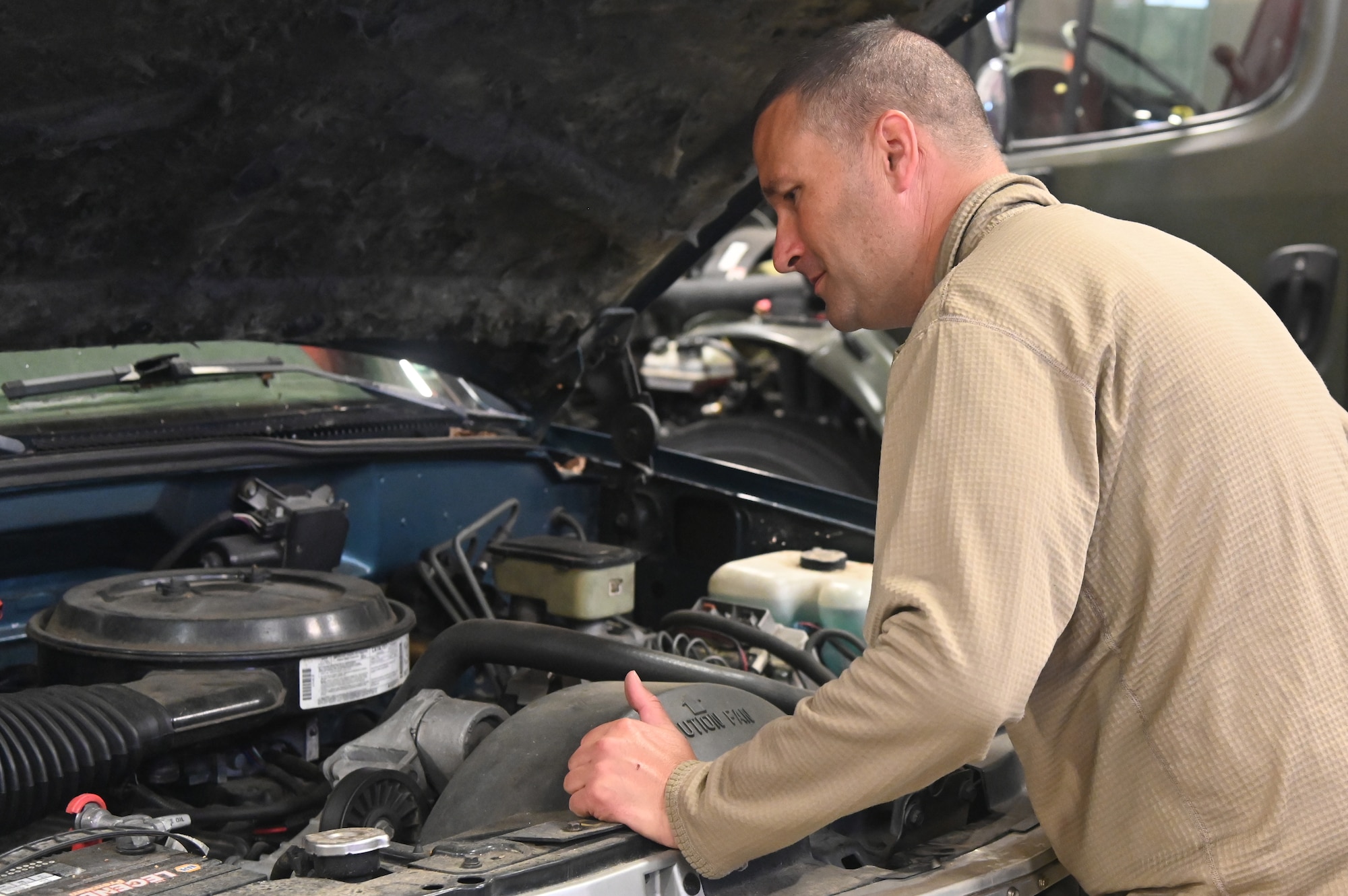 person looks under hood of vehicle