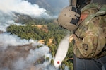 U.S. Army Staff Sgt. Kyle Sanders, a crew chief with G Company, 1st Battalion, 189th Aviation, watches as water releases from an HH-60M Black Hawk helicopter's bucket onto the Hagen Fire in Umatilla County, Oregon, Aug. 10, 2026. Photo by Maj. W. Chris Clyne.