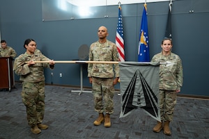U.S. Space Force Col. Angelo Fernandez (center), Mission Delta 3 commander, and Lt. Col. Danielle Ryan (right), 1st Electromagnetic Squadron (1 EWS) commander, look on as 1 EWS Senior Enlisted Leader Master Sgt. Hannah Friedrick (left) unfurls the squadron flag for the first time at a Peterson Space Force Base, Colorado ceremony, Aug. 3, 2026. Made up of primarily Guardians who transferred into the Space Force from the Air National Guard, 1 EWS marks a milestone in the implementation of the Space Force Personnel Act, which integrated legacy space units from the Air Force Reserve and Air National Guard into the Space Force. (U.S. Space Force photo by Dave Grim)