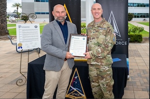 From left, Chris Pimentel, Mayor of El Segundo, Calif., presents a proclamation to USSF Col. Andrew Menschner, deputy commander, Space Systems Command (SSC), at Los Angeles Air Force Base in El Segundo, Calif. to commemorate the 5th anniversary of SSC’s stand up as a U.S. Space Force Field Command on Aug. 13, 2026. SSC is the Nation’s premier space acquisition organization responsible for fielding space-based capabilities that protect our Nation’s interests in, from and to space. SSC is headquartered at LA AFB with operating locations throughout the country including space launch operations at Cape Canaveral Space Force Station and Patrick Space Force Base in Fla. and Vandenberg Space Force Base in Calif. (U.S. Space Force photo by Chris Kim)