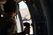 U.S. Air Force Staff Sgt. Devon Curtis, a special missions aviator assigned to Detachment 1, 413th Flight Test Squadron, looks at an HH-60W Jolly Green II assigned to the 88th Test and Evaluation Squadron while flying above Nellis Air Force Base, Nevada, April 29, 2025. Recently on Aug. 10, 2026, the 88 TES rapidly generated and deployed two HH-60W Jolly Green II helicopters to rescue five U.S. Navy personnel following an aircraft mishap near Naval Air Weapons Station China Lake, California. (U.S. Air Force photo by Staff Sgt. Jose Miguel T. Tamondong)
