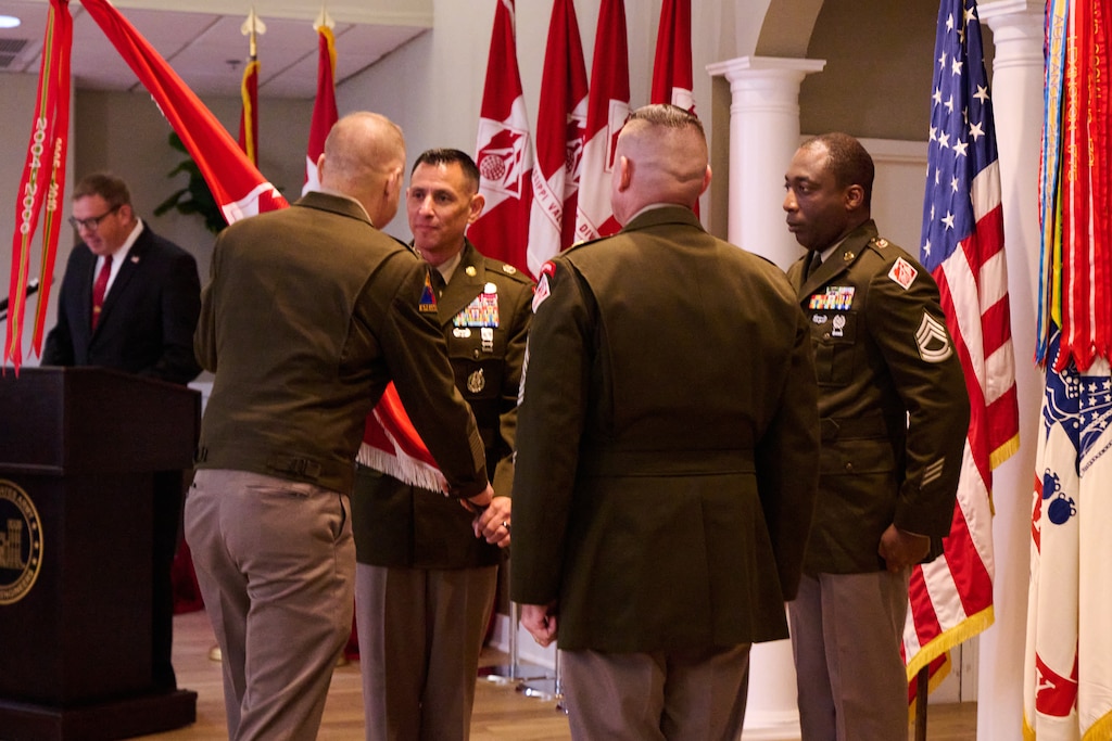 Two Soldiers are seen holding a flag as other Soldiers look on.