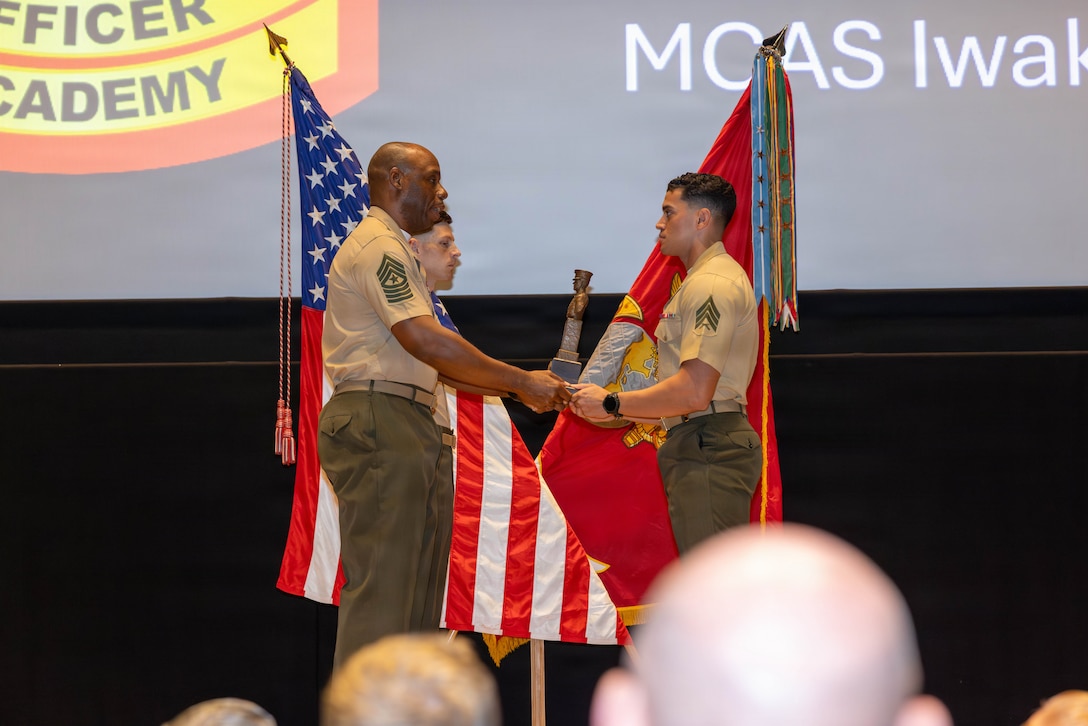 U.S. Marine Corps Sgt. Maj. Craig Provens, left, the sergeant major of Marine Fighter Attack Squadron (VMFA) 242, Marine Aircraft Group 12, 1st Marine Aircraft Wing, and native of San Antonio, Texas, presents the Gung Ho award to Sgt. Anthony Martinezarias, a mobile water supply operator with Headquarters and Headquarters Squadron (H&HS), Marine Corps Air Station Iwakuni, and a native of Hollywood, Florida, during the Sergeants School class 5-26 graduation at MCAS Iwakuni, Japan, Aug 11, 2026. The resident Sergeants School provided Marines aboard the installation with an opportunity to complete professional military education locally, strengthening leadership development and preparing them for increased responsibility within the Marine Corps. (U.S. Marine Corps photo by Lance Cpl. Isaac De Leon)