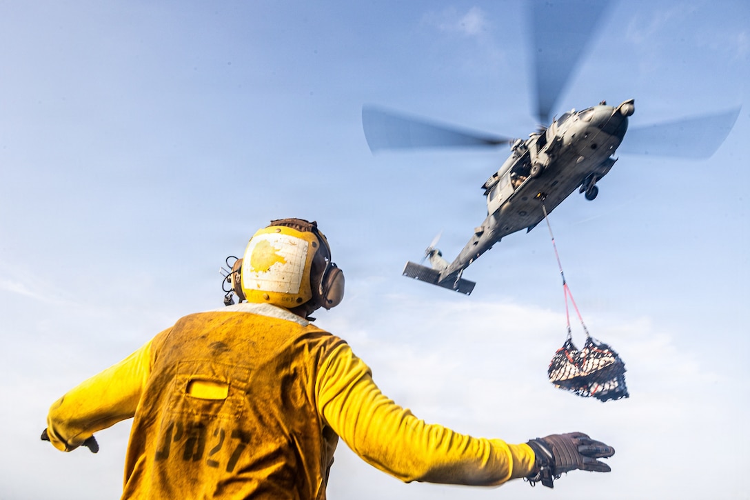 A U.S. Sailor assigned to San Antonio-class amphibious transport dock USS Portland (LPD 27) signals a Navy MH-60S Sea Hawk with Helicopter Sea Combat Squadron (HSC) 21 delivering pallets to the flight deck of Portland in the U.S. Central Command area of responsibility, August 8, 2026. (U.S. Marine Corps photo by Cpl. Avery Wayland)