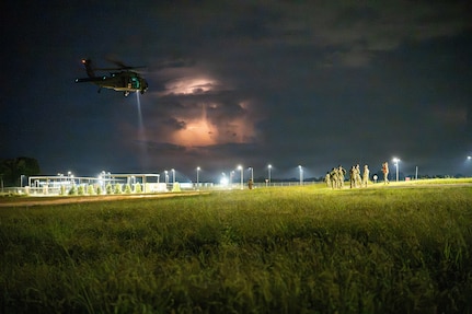 An Alabama Army National Guard UH-60 Black Hawk helicopter conducts nighttime operations during Operation Tuskegee Thunder at Dannelly Field, Alabama, Aug. 13, 2026, as lightning illuminates a storm in the distance.