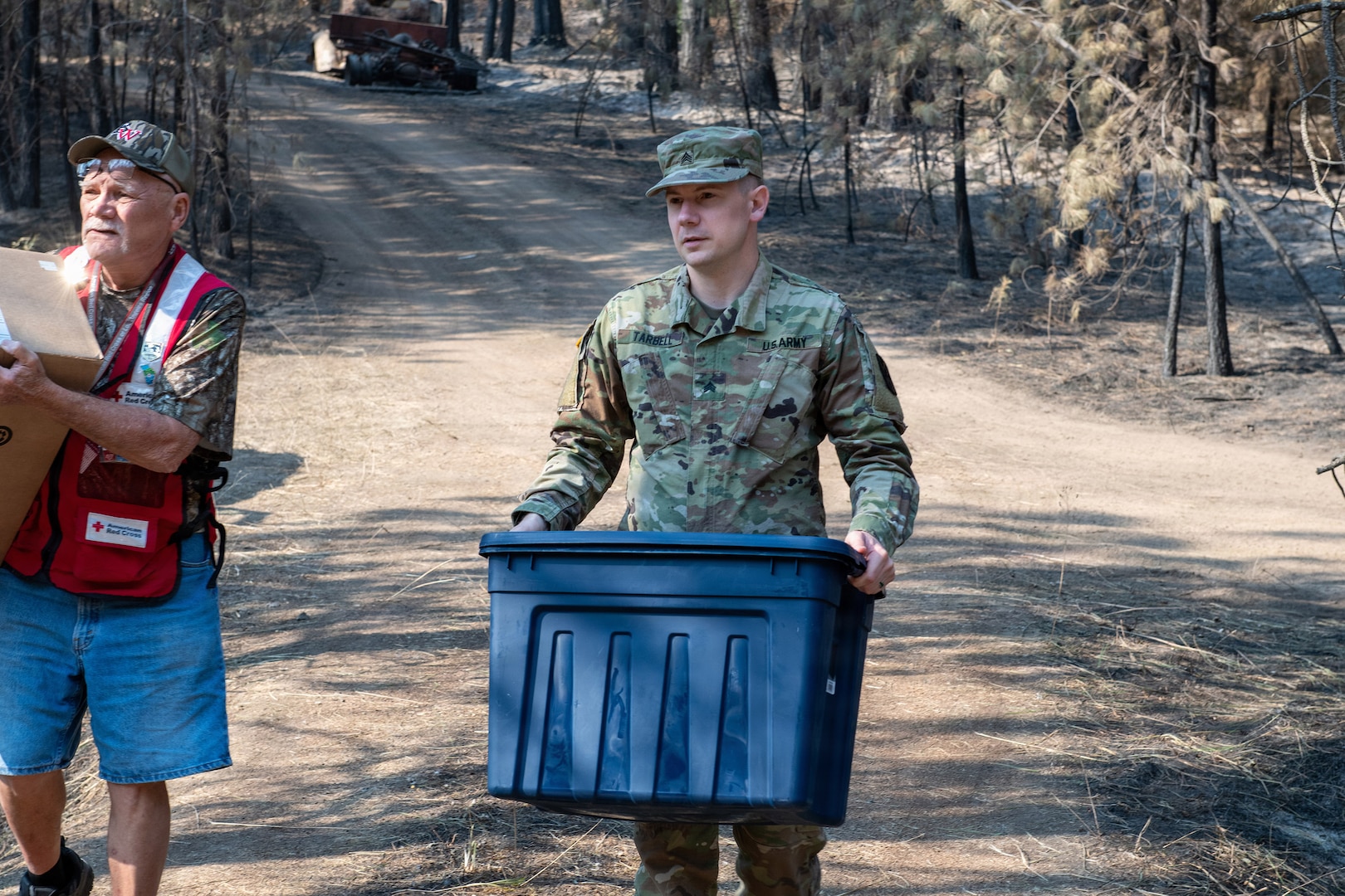 Washington Army National Guard Sgt. Keegan Tarbell, assigned to the 341st Military Intelligence Battalion, carries an emergency relief package alongside an American Red Cross volunteer during the Spokane-area wildfire response in Spokane, Wash., Aug. 11.