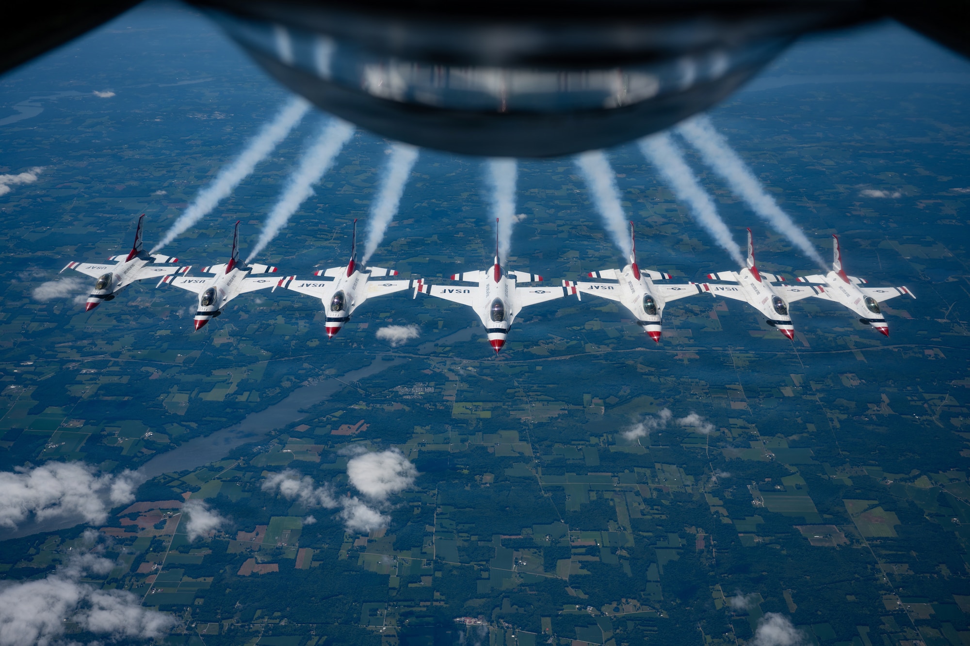Seven white planes with smoke coming from the engines flying behind a KC-135 Stratotanker
