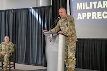 Photo of COL Kilgore at a podium and Depot SGM Alkire sitting in the background