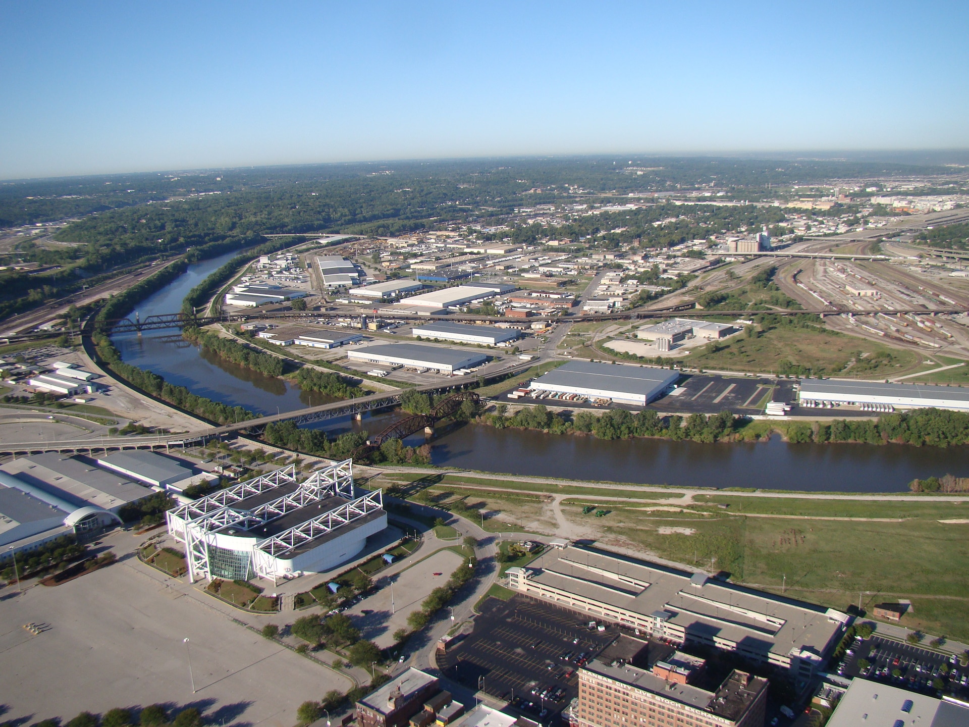 A brown river cuts through a city with buildings and grass on either side and two bridges crossing it.