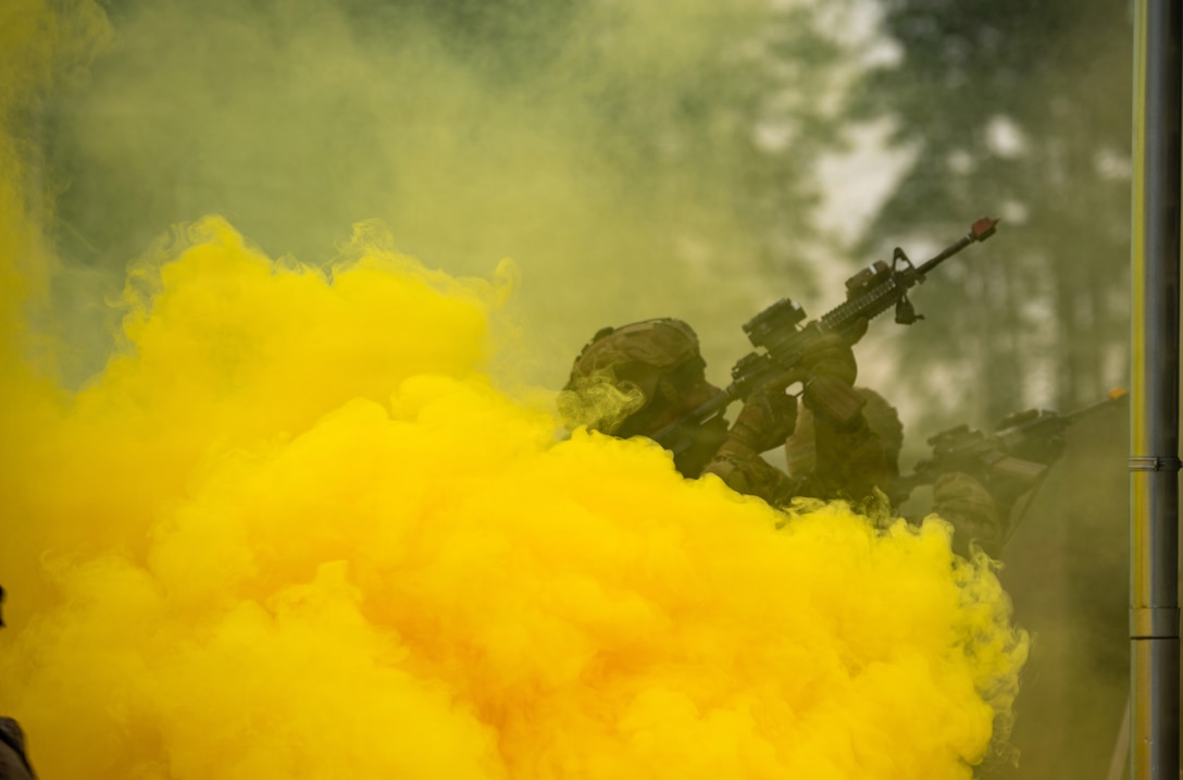 A soldier aims a weapon upward while mostly obscured by a thick cloud of yellow smoke.