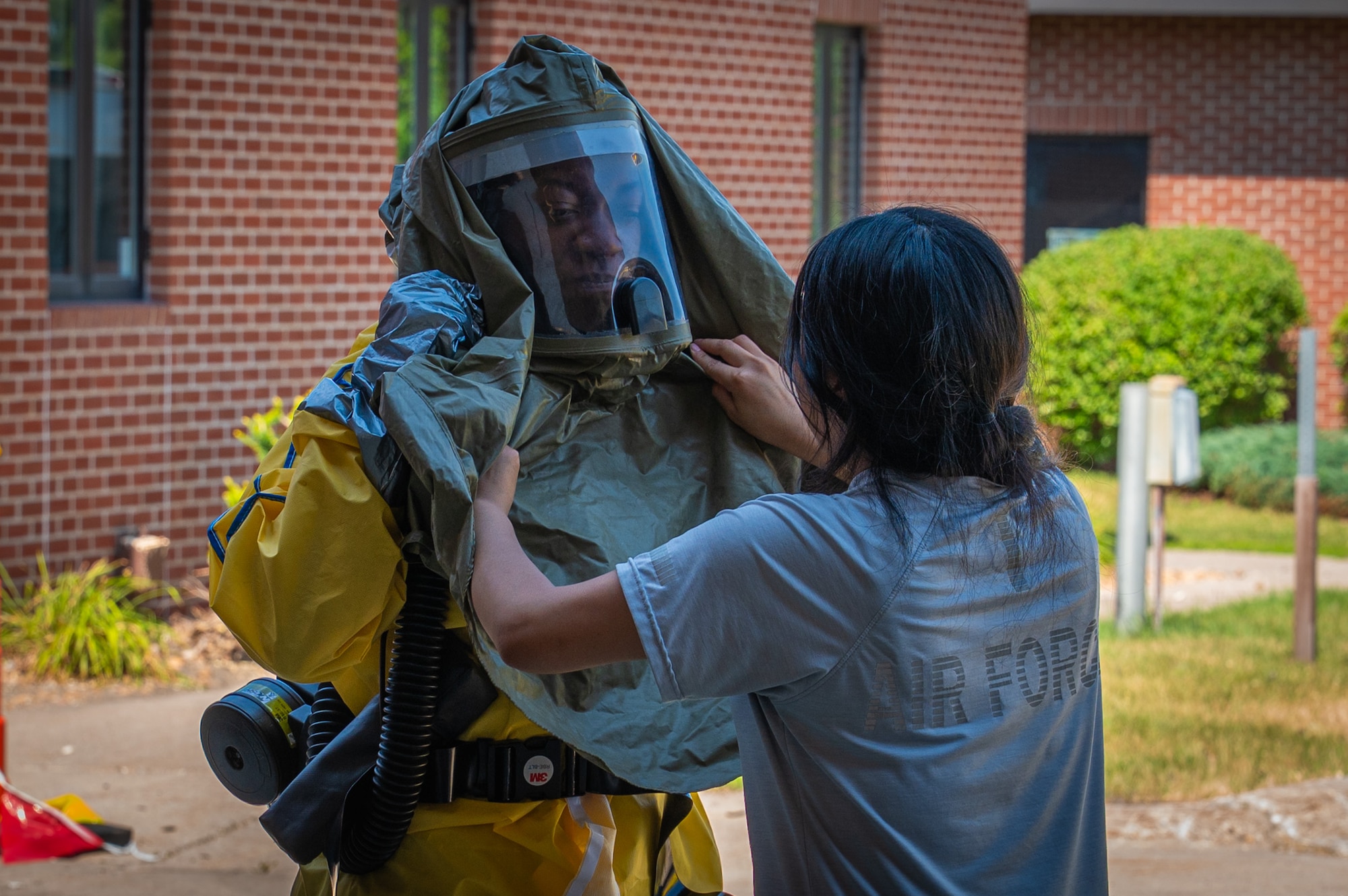 A photo of a woman helping another woman don a hazardous material suit.