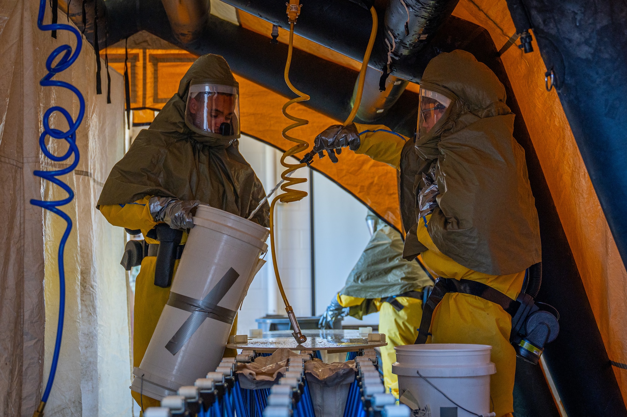 A photo of two people standing in a medical tent filling up a bucket with water.