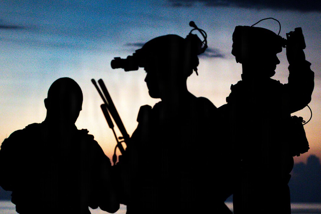 Three Marines shown in silhouette adjust personal protective equipment they're wearing outdoors.