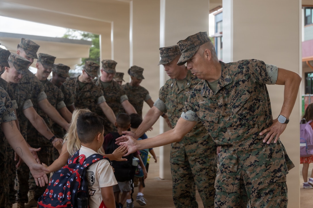 U.S. Marine Corps Col. Stephen DeTrinis, commanding officer of Marine Corps Base Hawaii, left, and Sgt. Maj. Adan Moreno, senior enlisted leader of MCBH, greet children during the first day of school celebration at MCBH, Aug. 5, 2026. This event welcomed students back to the classrooms, provided extra motivation and strengthened the bonds between the Marines and the MCBH community. (U.S. Marine Corps photo by Lance Cpl. Nicholas Figueroa)
