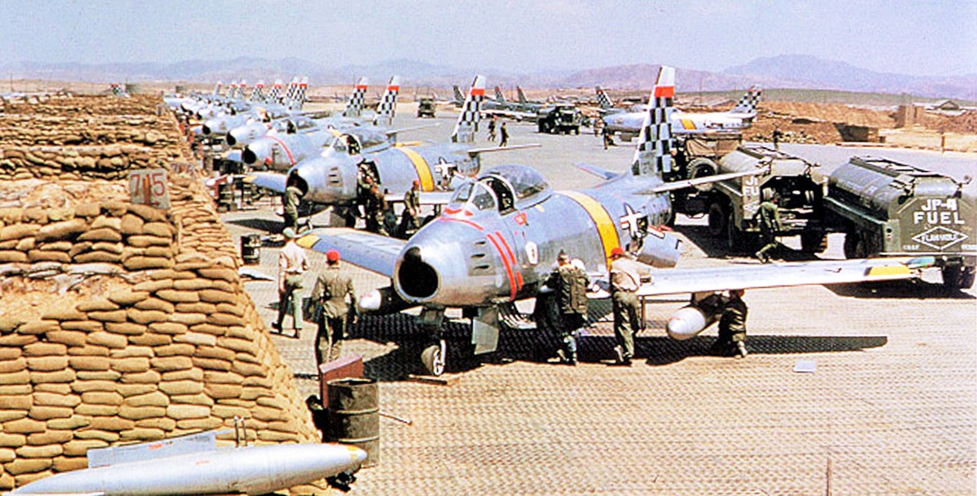 Crew chiefs and ground personnel service a long lineup of 51st Fighter-Interceptor Wing F-86 Sabres in sandbagged revetments at Suwon Air Base, South Korea, circa June 1953.