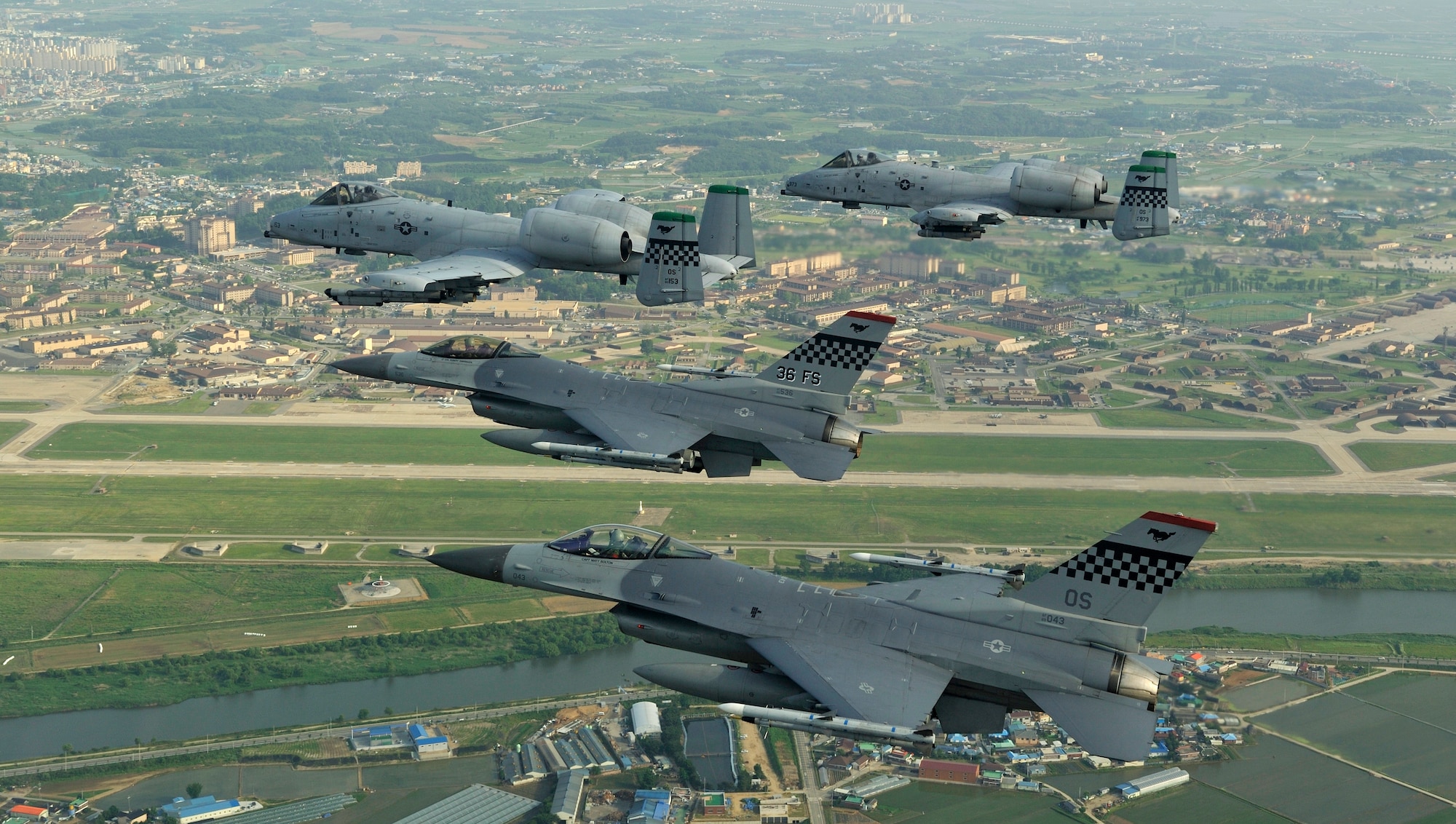 Two F-16 Fighting Falcons from the 36th Fighter Squadron fly alongside two A-10 Thunderbolt IIs from the 25th Fighter Squadron during a four-ship "checkertail" flyover of Osan Air Base, South Korea, circa 2009. This mixed-fleet pairing served as the cornerstone of the peninsula's air defense for decades.