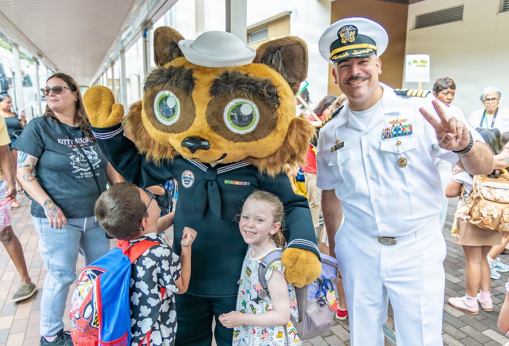 IKEGO HILLS FAMILY HOUSING AREA, Japan (Aug. 17, 2026) - Capt. Jon Hopkins, Commander, Fleet Activities Yokosuka (CFAY), right, and installation mascot Yoko-Pon pose with students outside Ikego Elementary School on the first day of school, Aug. 17, 2026. Base leadership visited the campus to support returning families and underscore the installation’s partnership with Department of War Education Activity (DoWEA) schools. CFAY provides, maintains, and operates base facilities and services in support of the U.S. 7th Fleet's forward-deployed naval forces, 71 tenant commands, and more than 27,000 military and civilian personnel and their families.  (U.S. Navy photo by Sheryl Sullivan)