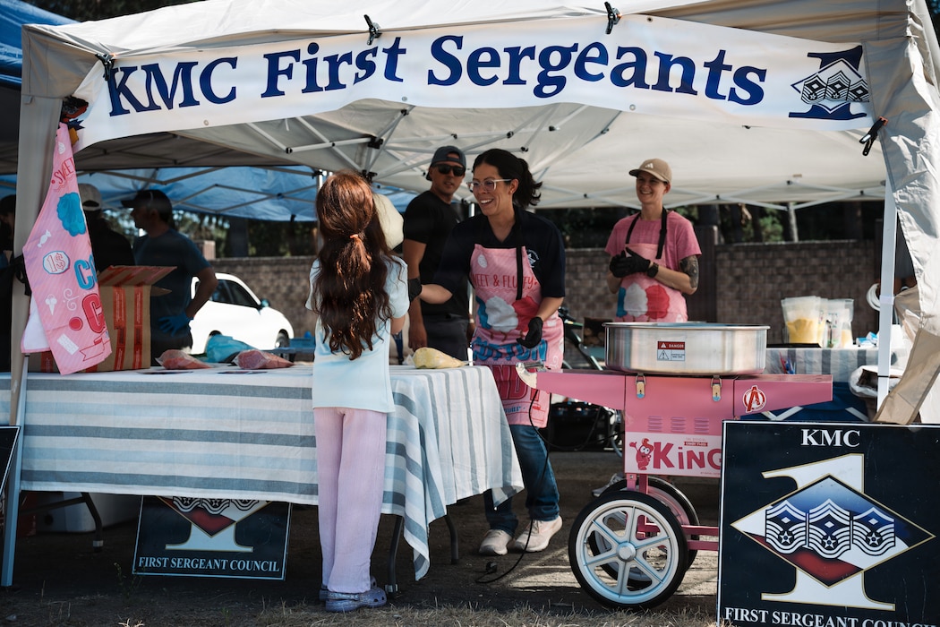U.S. Air Force Master Sgt. Valerie Groupp, center, 1st Engineering Installation Squadron first sergeant, hands cotton candy to a child during the Chapel Carnival at Ramstein Air Base, Germany, Aug.14, 2026.