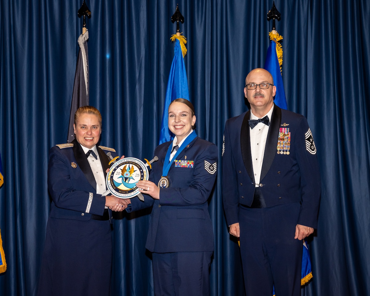 A female Airman is presented an award by a female and male Airman.