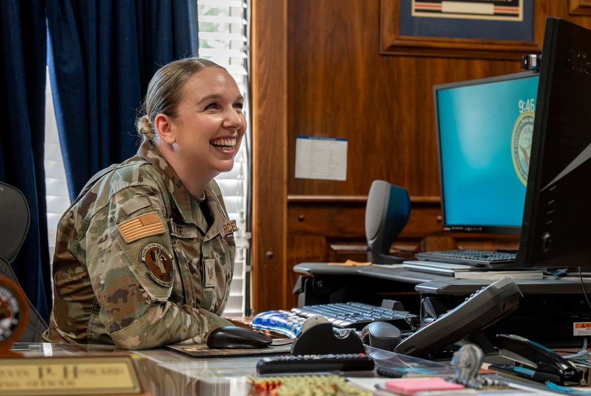 A female Airman smiles while sitting at a computer.