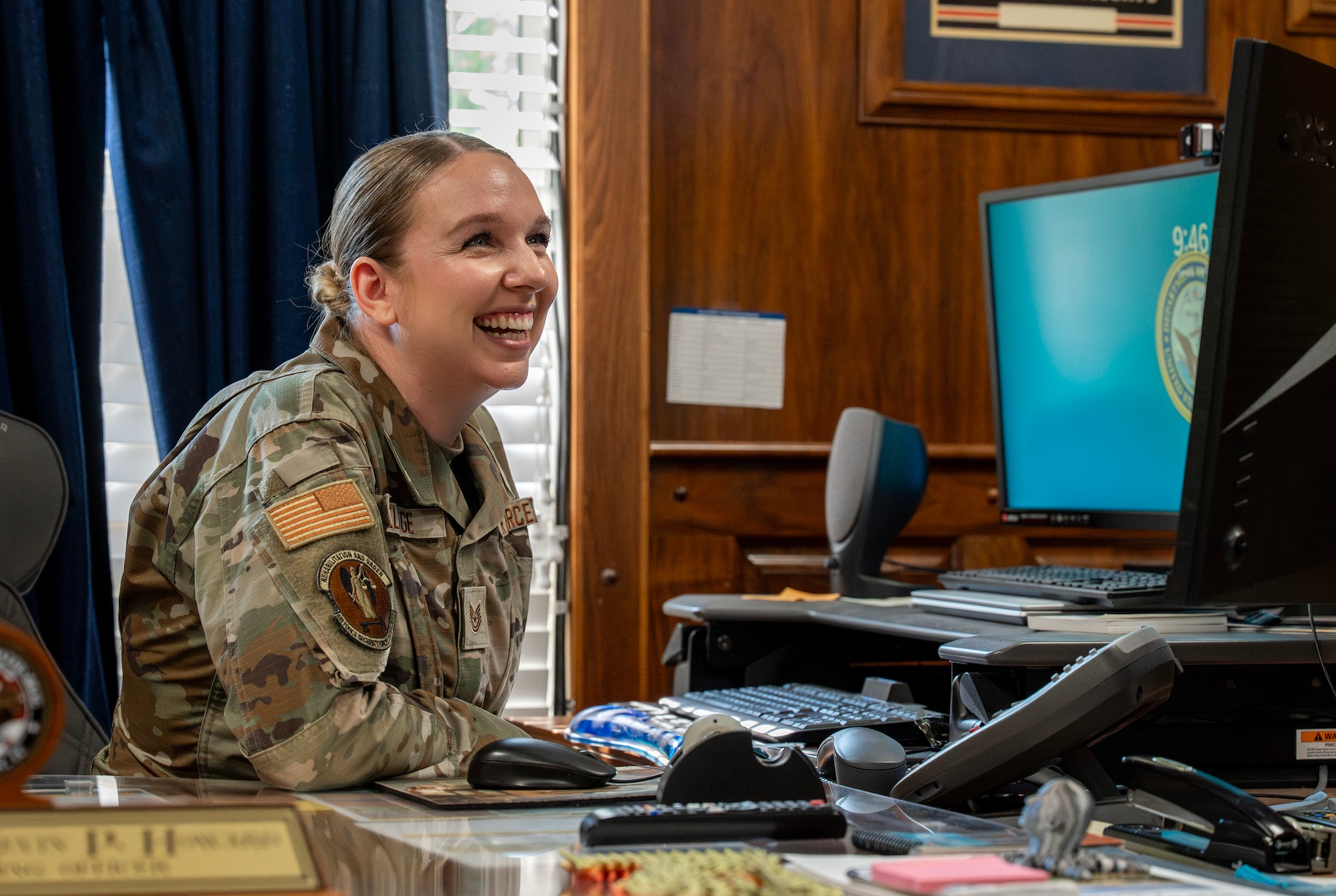 A female Airman smiles while sitting at a computer.
