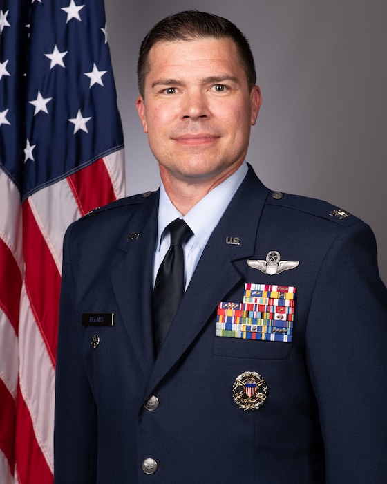 An Air Force Colonel poses for an official military photo, an American flag position to his left.