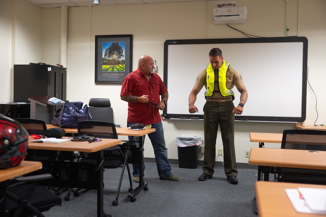 Mark Dumdie, 17th Training Wing Safety motorcycle safety program manager, and U.S. Marine Corps Sgt. Alejandro Clausell, Marine Detachment Goodfellow motorcycle mentorship program president, demonstrate how an airbag vest deploys during a motorcycle safety meeting at Goodfellow Air Force Base, Texas, Aug. 14, 2026. The Air Force Safety Center sent the 17th TRW a demonstration vest with reloadable gas cartridges to educate motorcyclists and bring awareness to safety technologies that are available to them in the event of a motorcycle mishap. (U.S. Air Force photo by Senior Airman Brian Lummus)