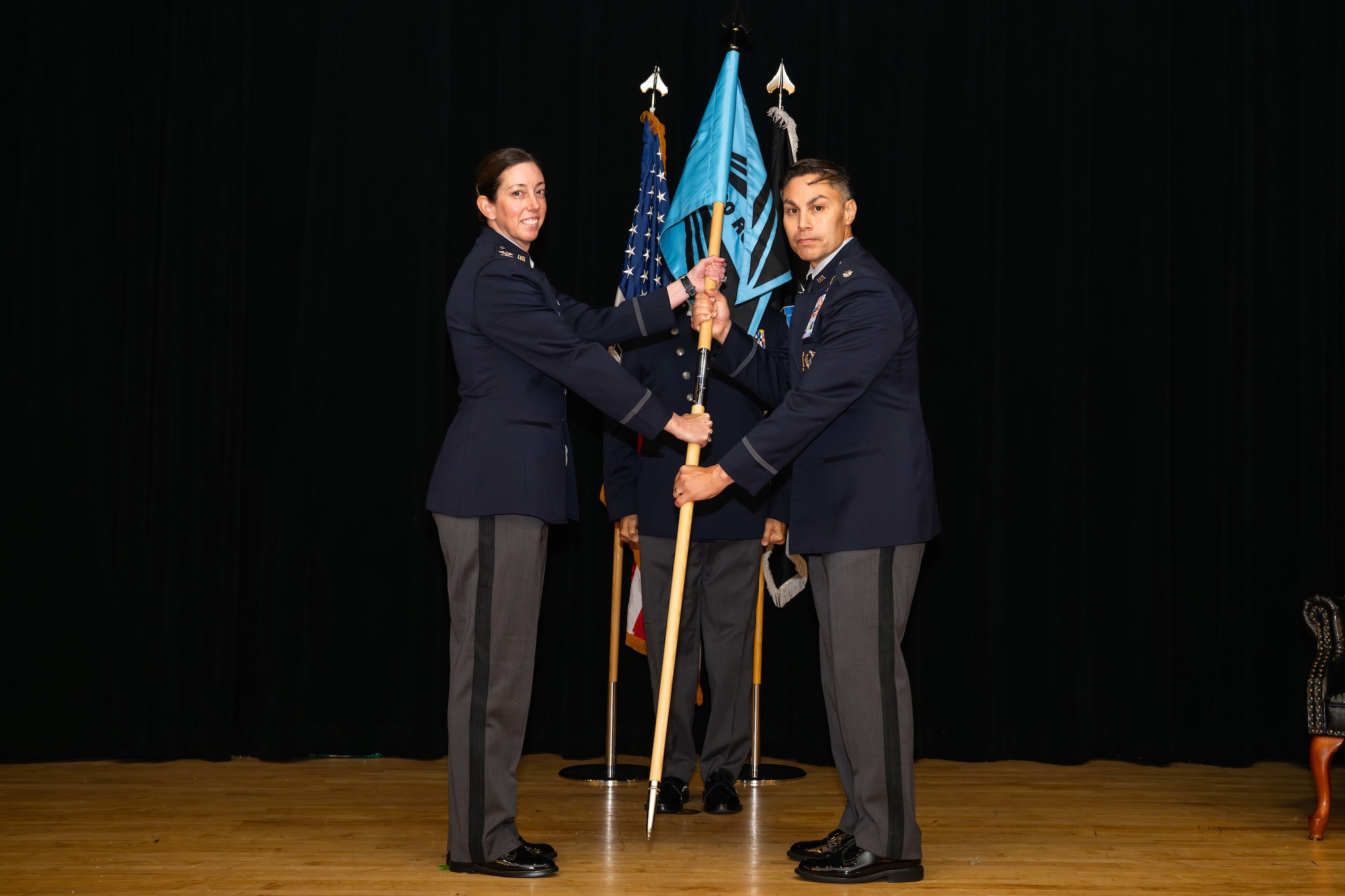 Man and woman in uniform with flag on stage