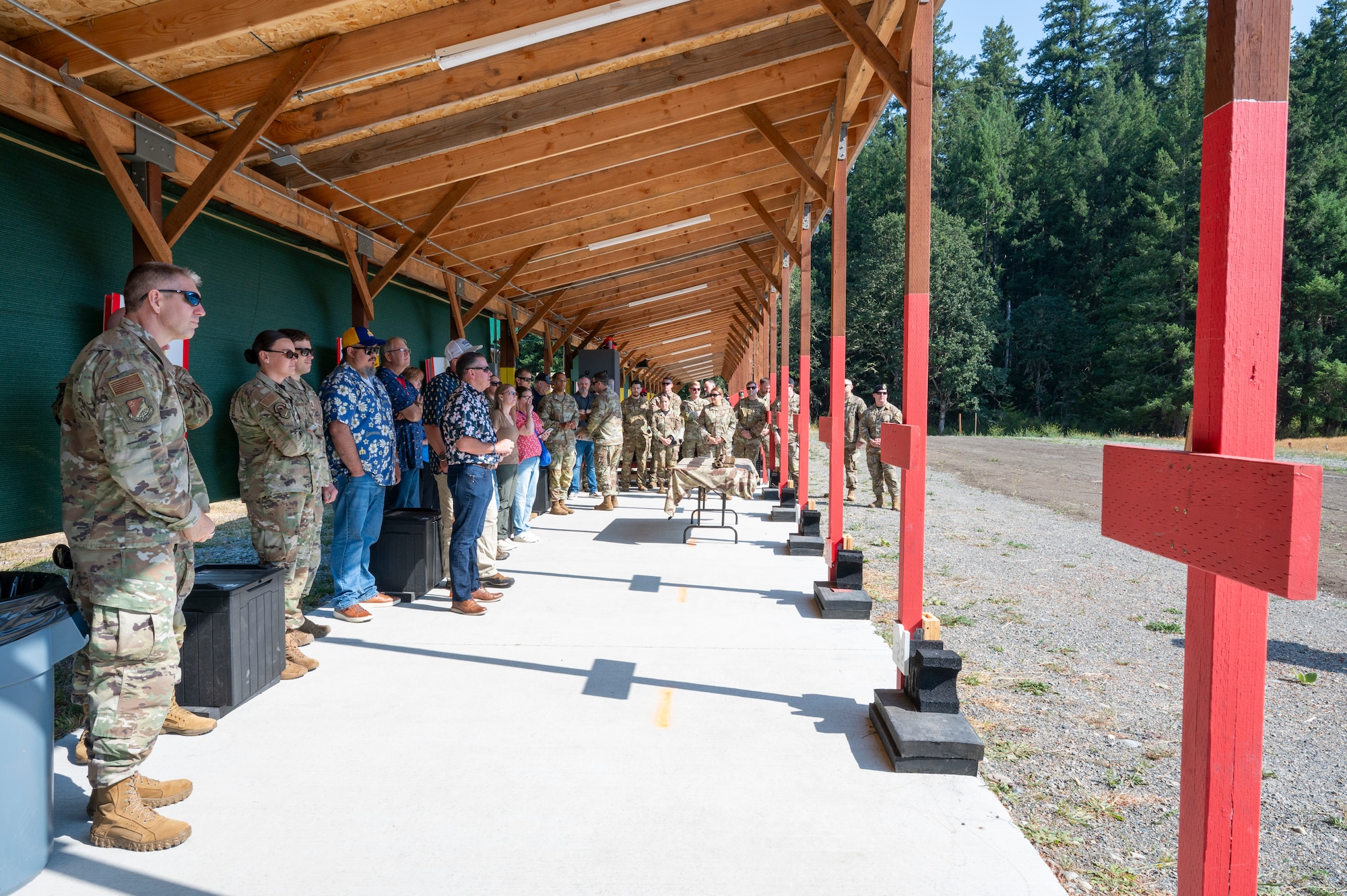 A group of people stand under a shooting range and listen to a speaker.