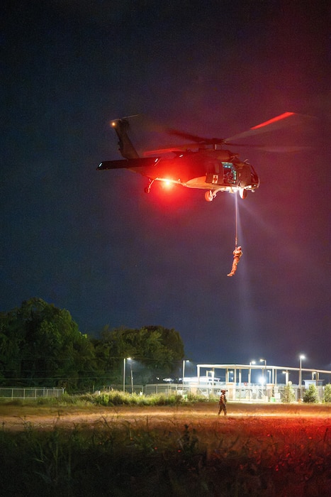 A UH-60 Black Hawk helicopter hoists a service member at night.